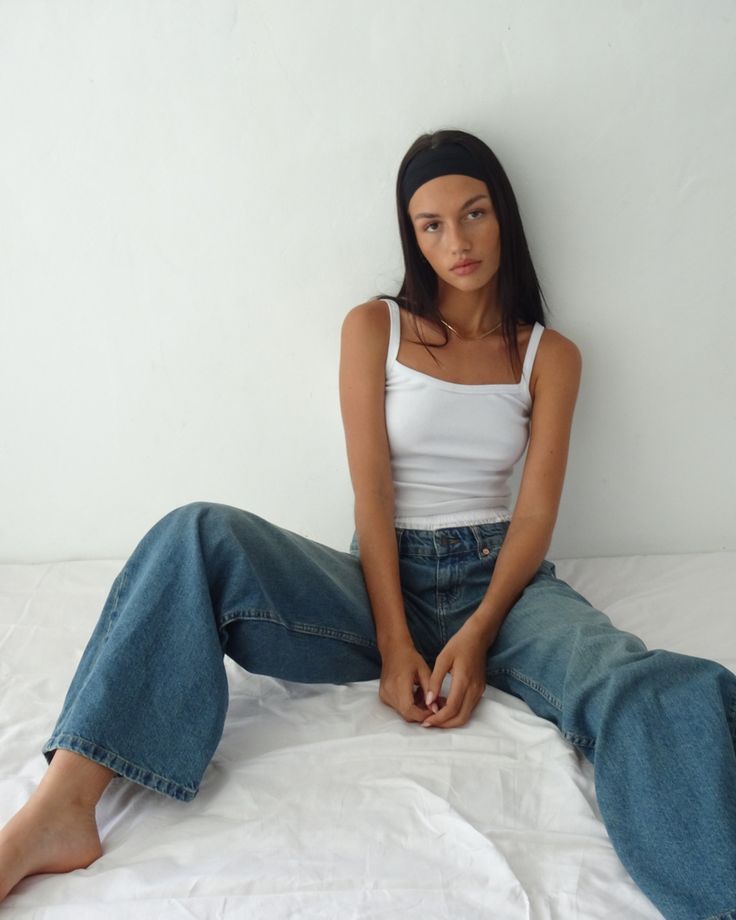 a woman sitting on top of a bed wearing jeans