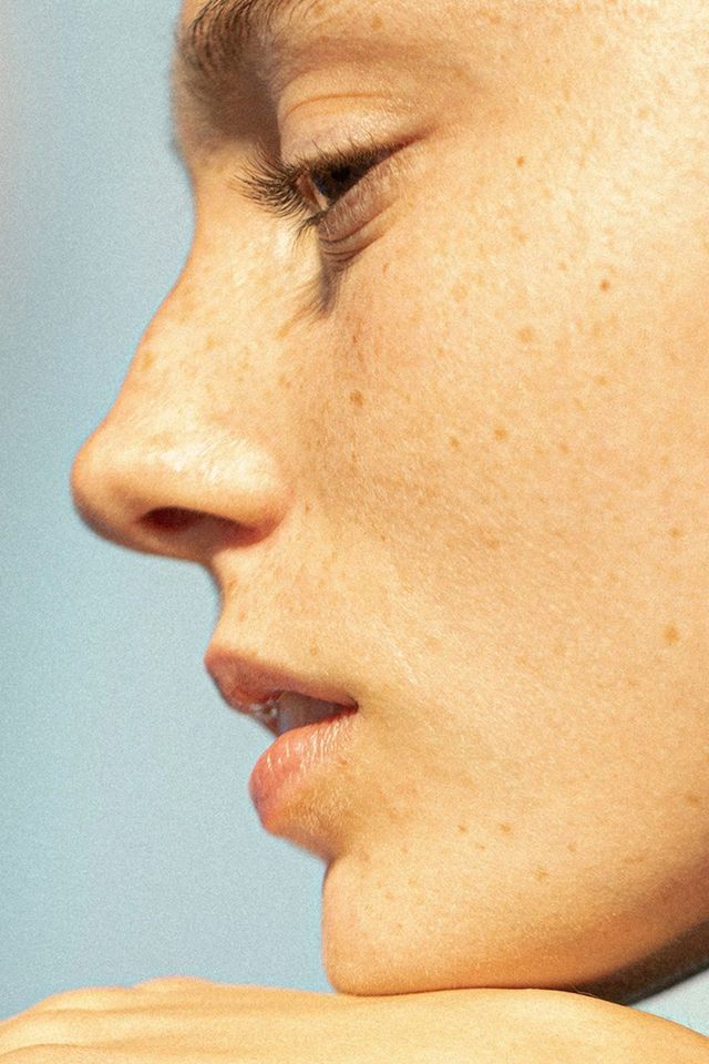 a woman with freckles on her neck looking to the side while she is brushing her teeth