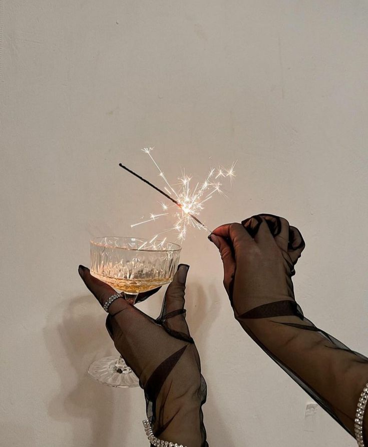 two hands holding a wine glass with sparklers in it