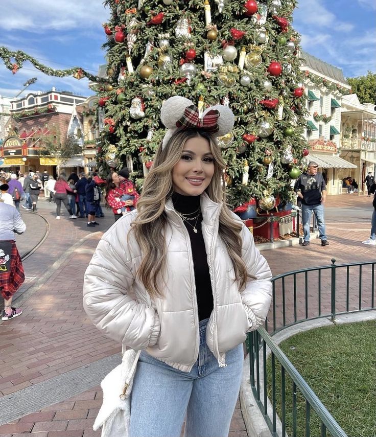 a woman standing in front of a christmas tree wearing minnie mouse ears on her head