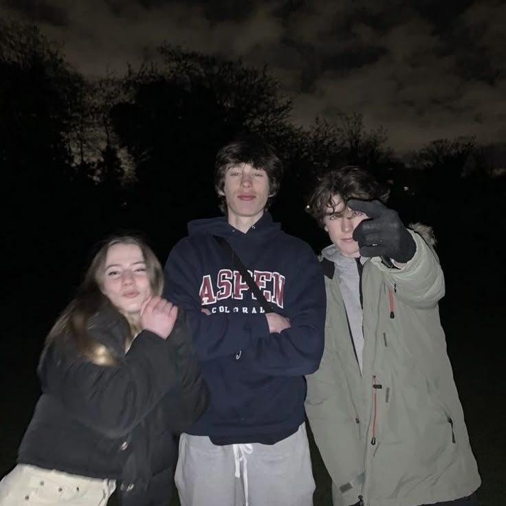 three young people standing next to each other in front of the dark sky at night