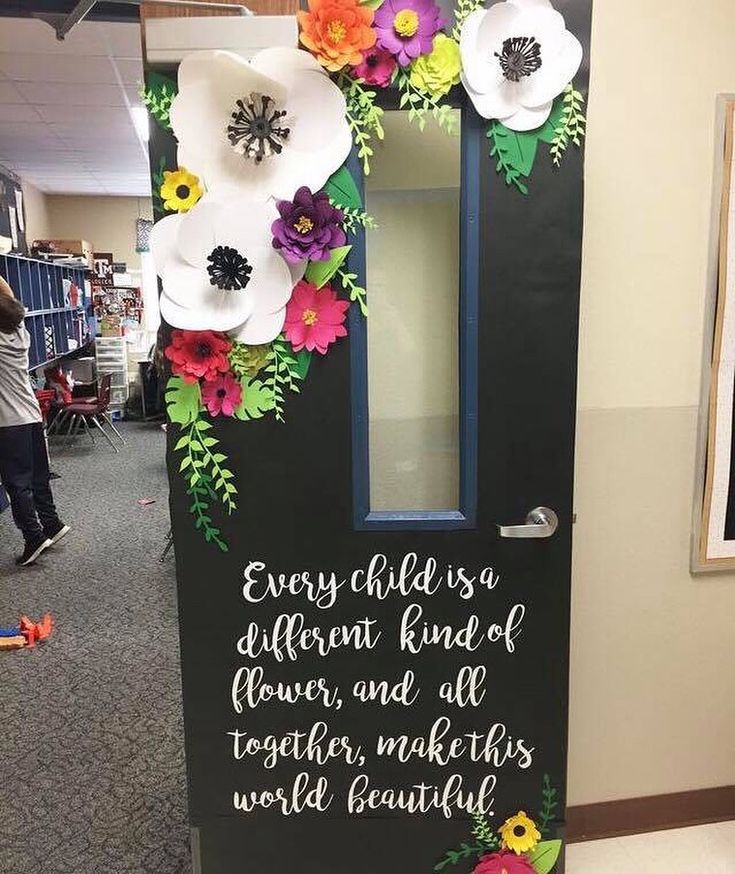 a door decorated with paper flowers and writing on the front, says every child is a different kind of flower, and all together makes world beautiful