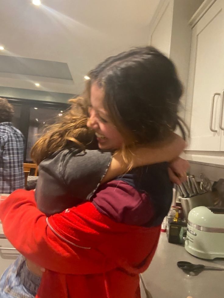 two women hug in the kitchen while another woman watches