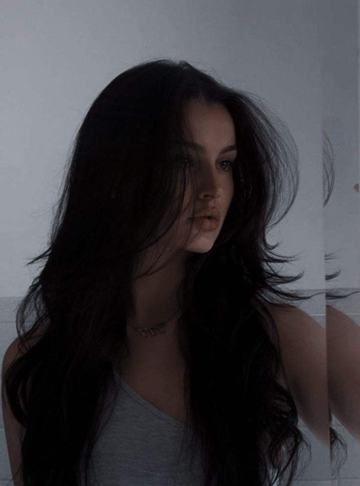 a woman with long black hair standing in front of a mirror