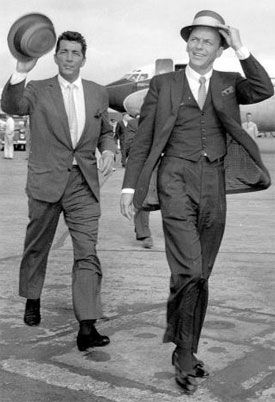 two men in suits and hats walking on an airport tarmac, one carrying a hat