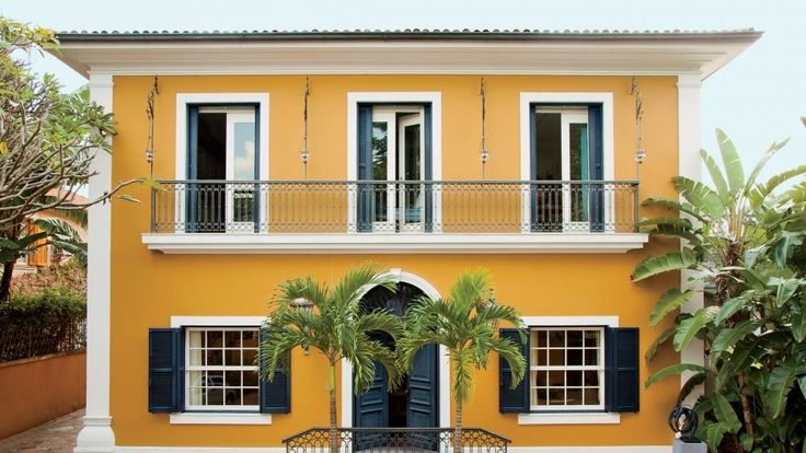 a yellow house with black shutters and palm trees