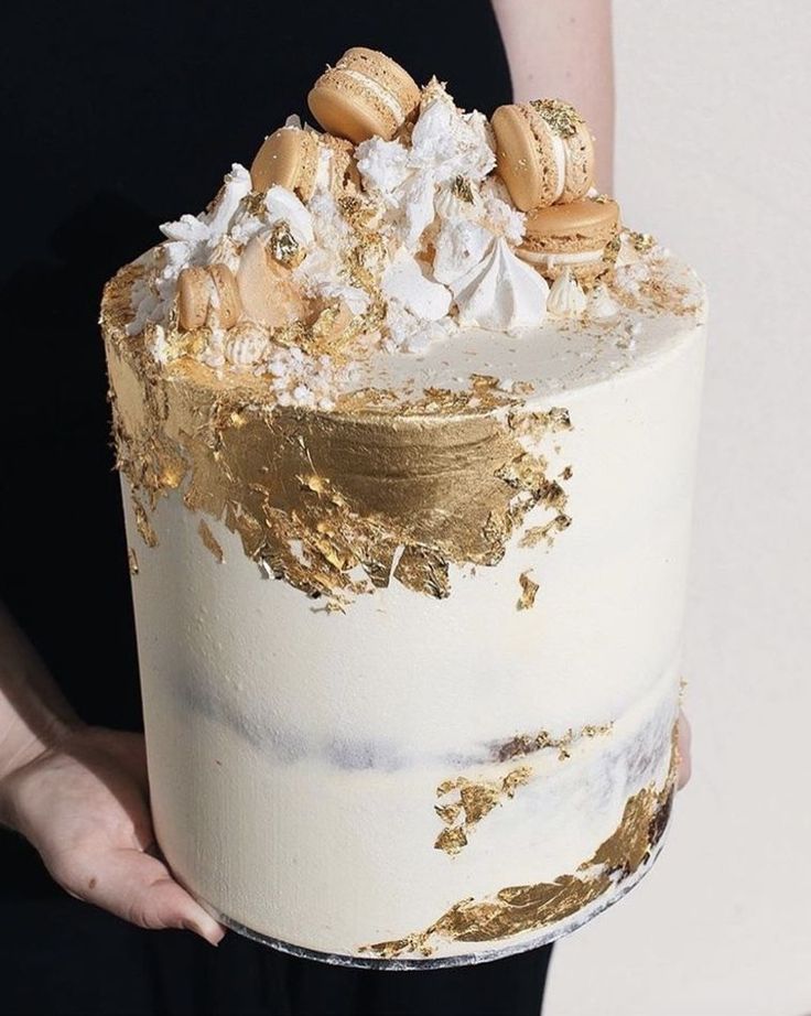 a person holding a cake with gold and white frosting on it's side