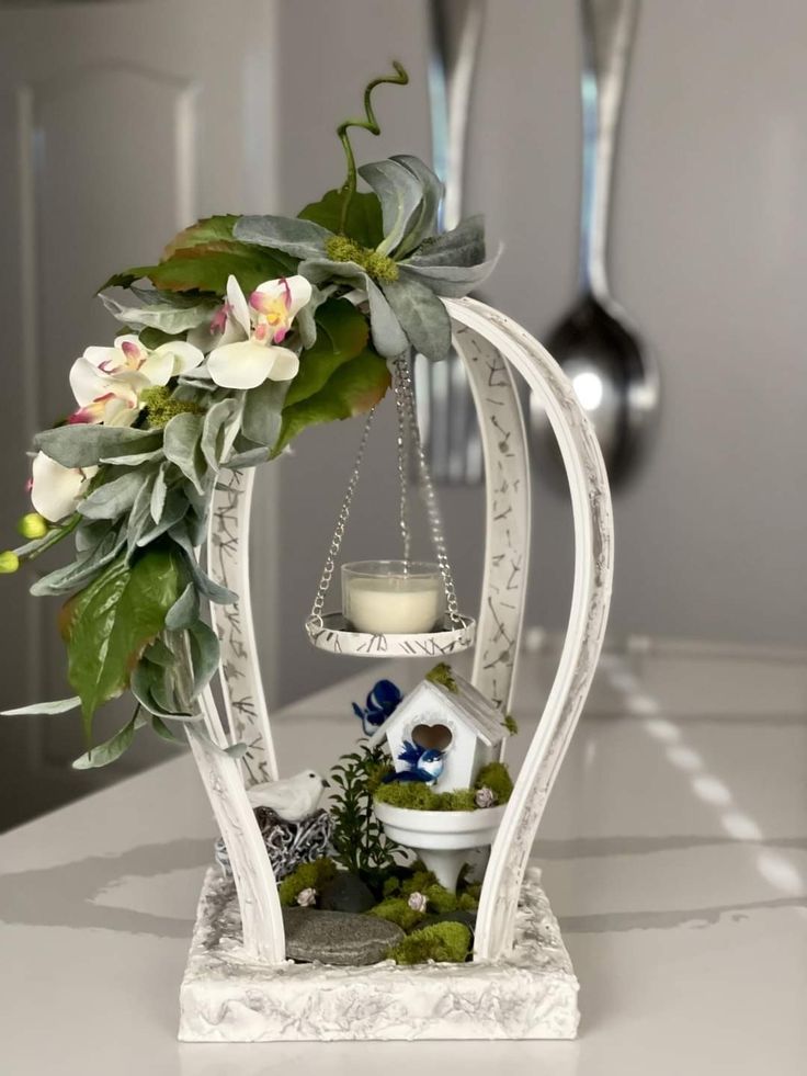 a white vase with flowers and a candle on it sitting on top of a table