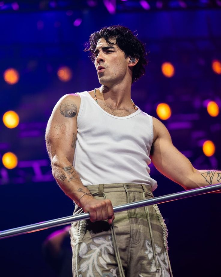 a man with tattoos on his arm holding a metal pole in front of purple lights