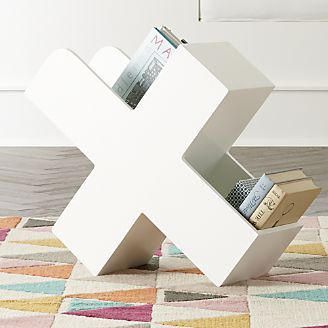 a white book holder with books in it on a colorful rug next to a wall