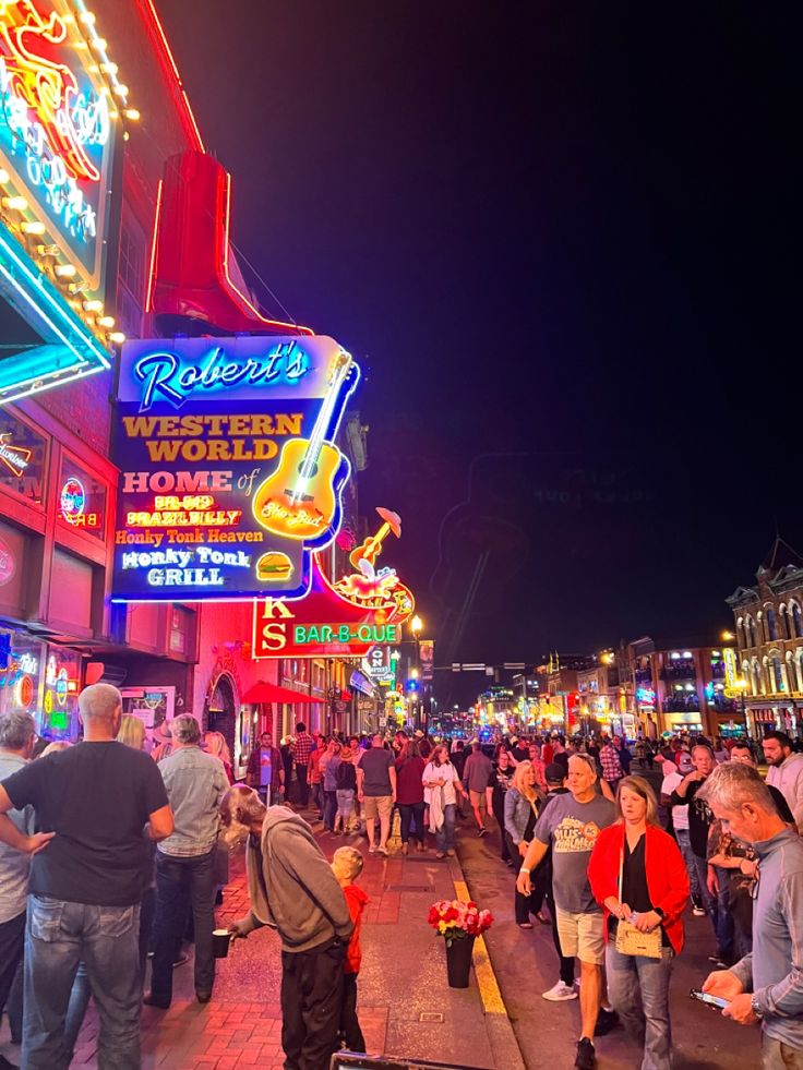 many people are walking down the street in front of neon signs and buildings at night