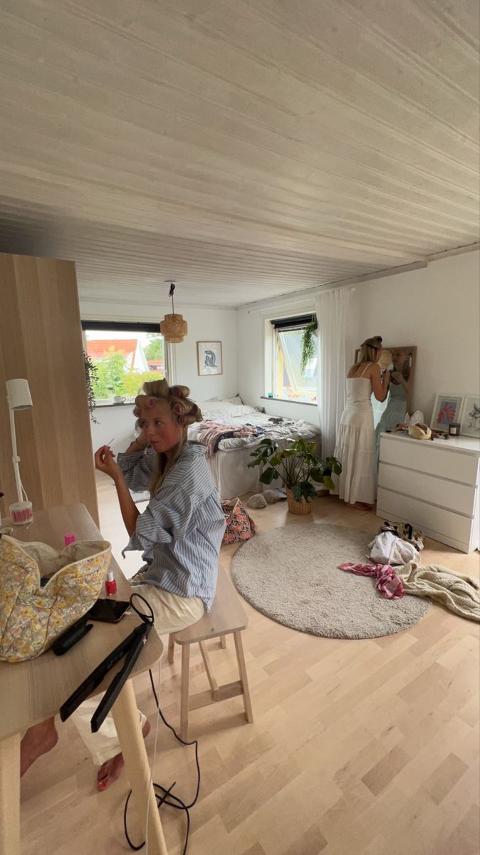 a woman sitting on a stool in a room with wood flooring and white walls