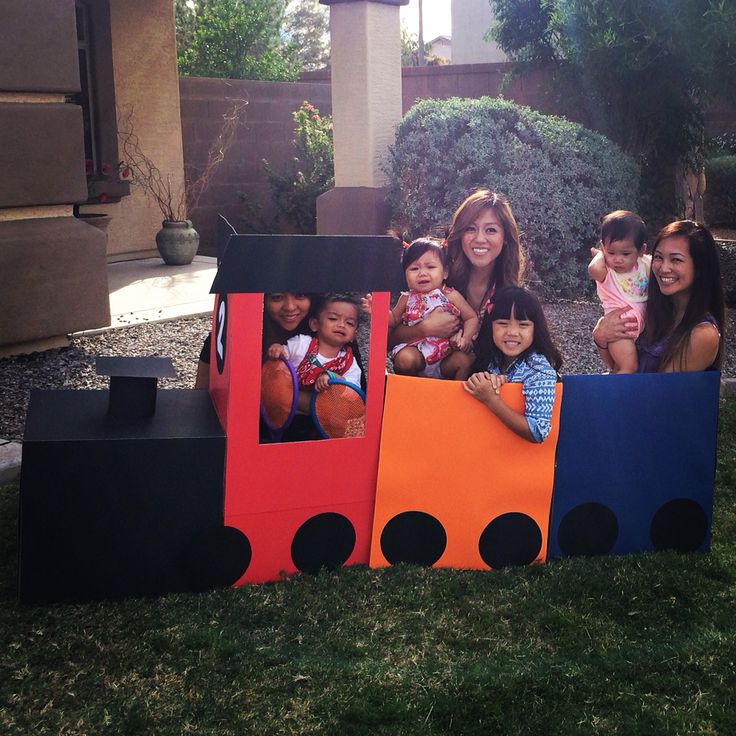 a group of people that are sitting in a train shaped cardboard box on the grass