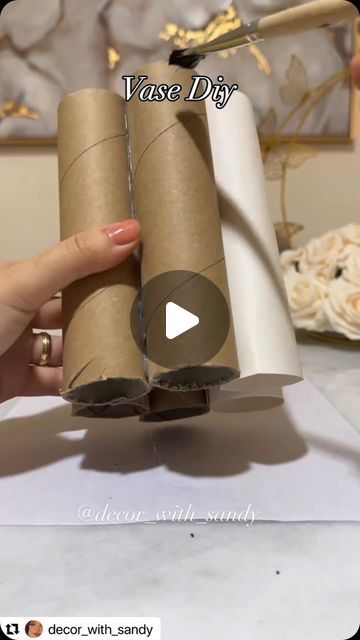 a person holding two rolls of toilet paper in front of a flower arrangement with the words vase diy on it