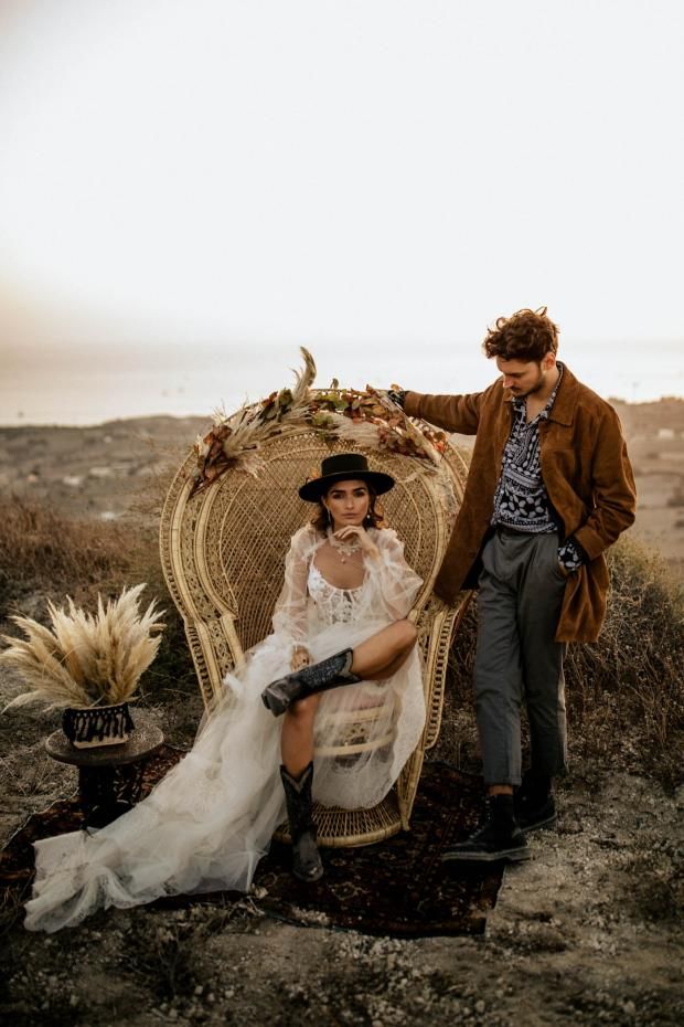 a man standing next to a woman in a white dress sitting on a wicker chair