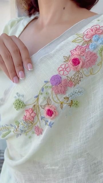 a woman with pink nails is wearing a white shirt and has flowers on the sleeves