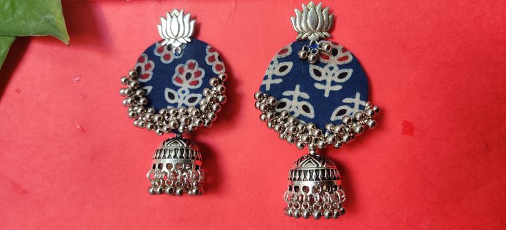 two pairs of earrings with bells hanging from them on a red surface next to a plant