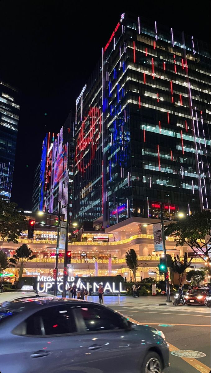 a car is driving down the street in front of some tall buildings with colorful lights on them