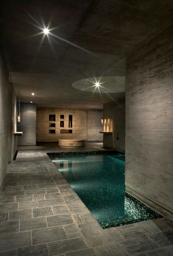 an indoor swimming pool in a house with stone flooring and walls, surrounded by lights