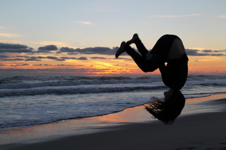 a person doing a handstand on the beach at sunset