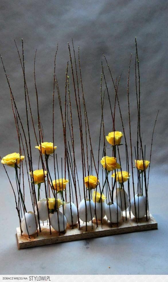 some yellow flowers and white eggs are arranged on a wooden stand with thin stems in the center