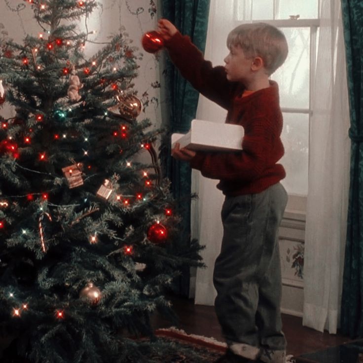 a young boy holding a present near a christmas tree