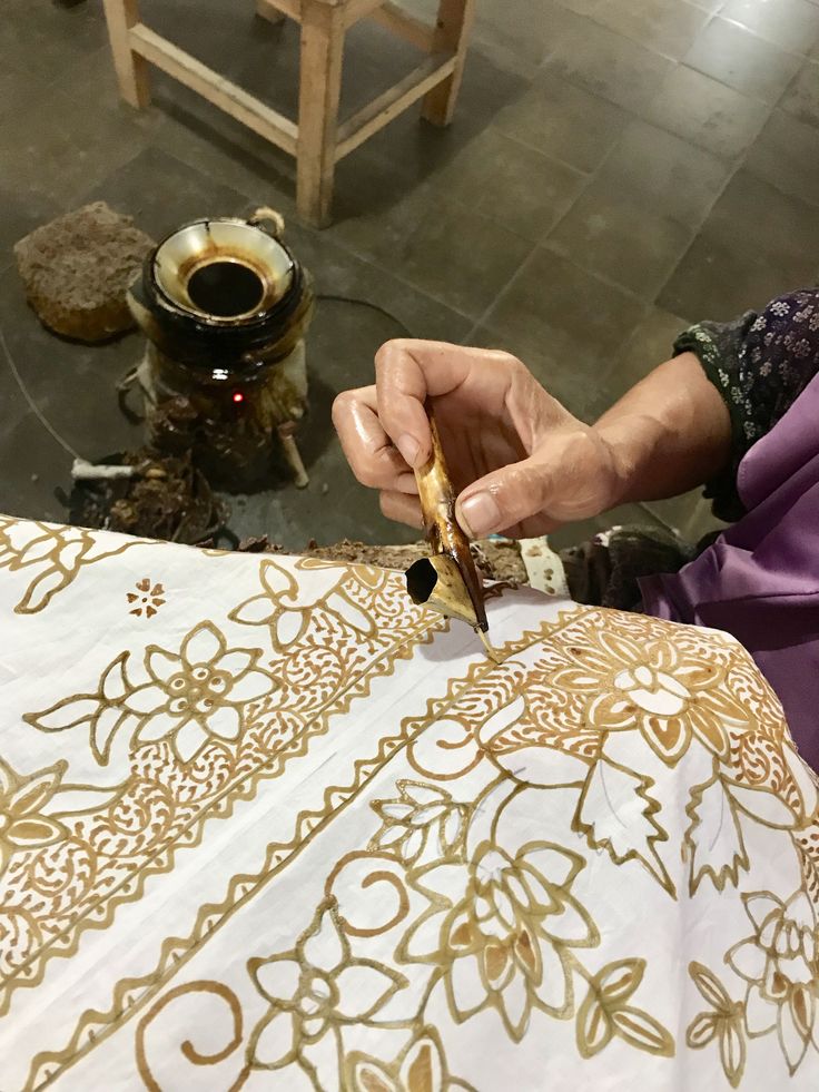 a woman is working on an intricately designed table cloth with gold and white designs