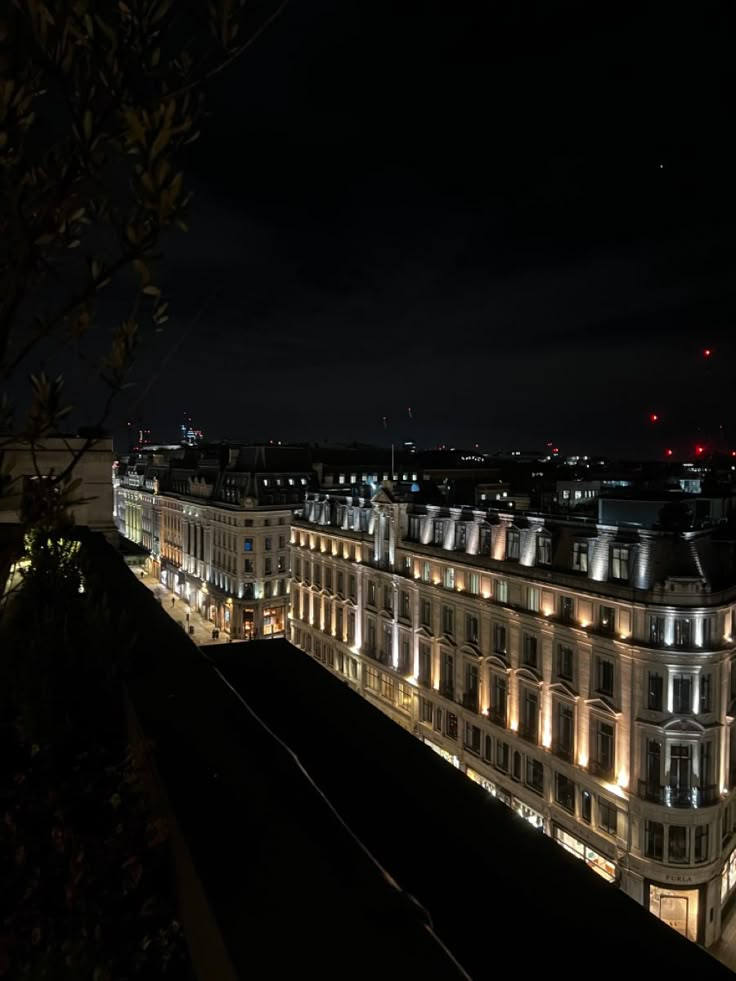 the city lights shine brightly at night in this view from an apartment building's roof