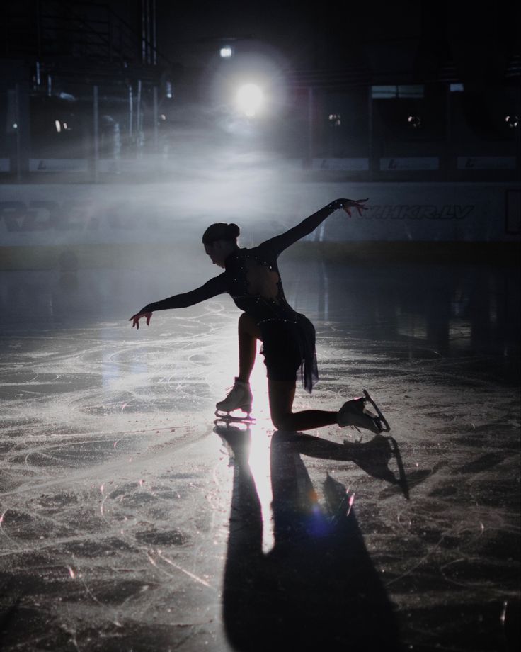 a person skating on an ice rink at night with the light from behind them shining