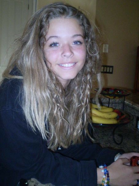 a woman with long blonde hair sitting in front of bananas on a counter top and smiling at the camera