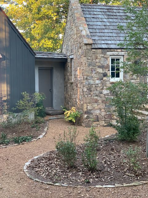 a stone house in the middle of a wooded area with trees and shrubs around it