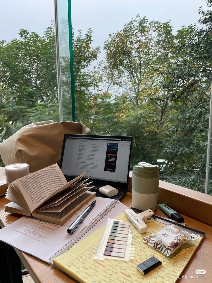 an open book sitting on top of a desk next to a laptop computer and cup