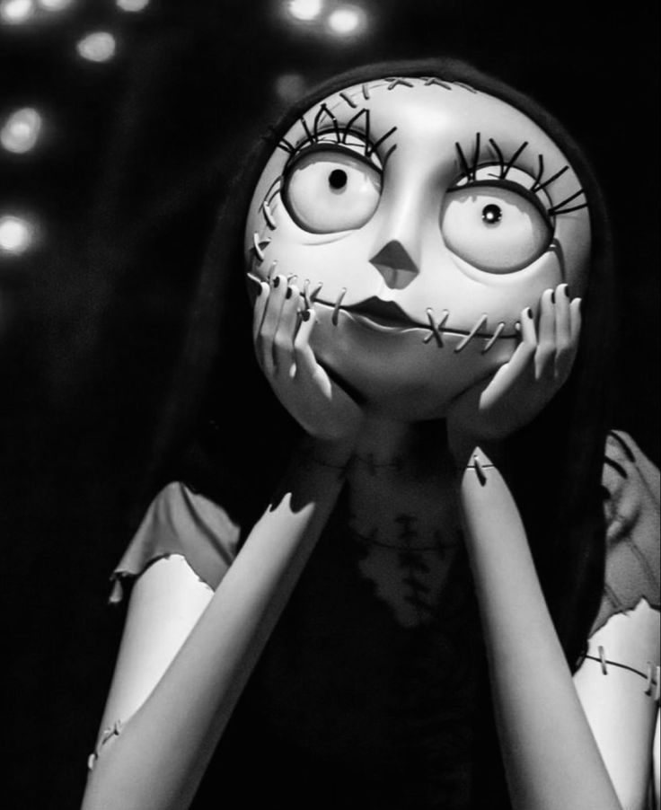 a black and white photo of a creepy doll with eyes, hands on her face