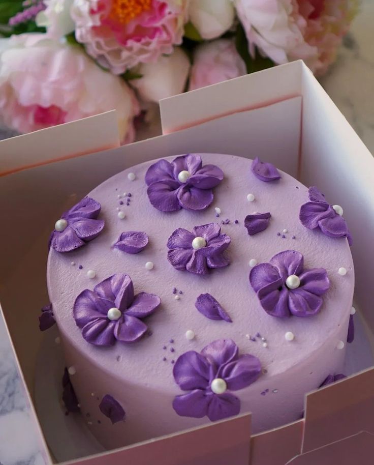 a purple cake in a pink box with flowers on the top and pearls around the edges