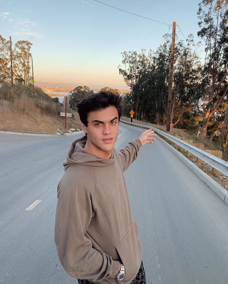 a young man standing on the side of a road with his hand in the air