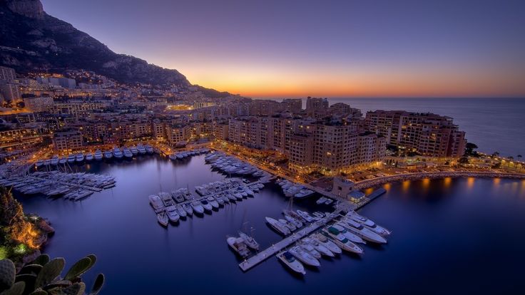 an aerial view of boats docked in the harbor at night, with mountains in the background