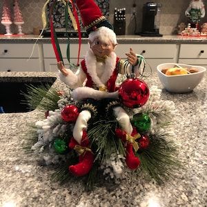 an elf is sitting on top of a christmas tree in the middle of a kitchen