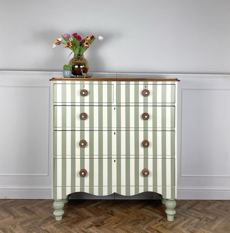 a striped chest of drawers with flowers in a vase sitting on it's top