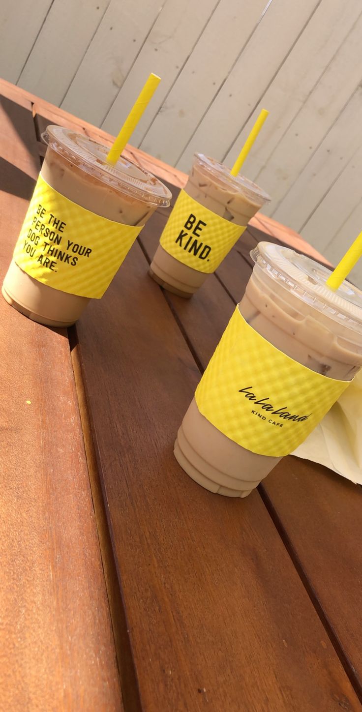 three cups of coffee sitting on top of a wooden table with yellow straws in them