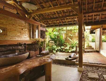 an outdoor bathroom with stone flooring and wooden walls, surrounded by greenery in the background