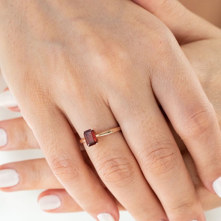 a woman's hand wearing a gold ring with a garnet colored stone on it