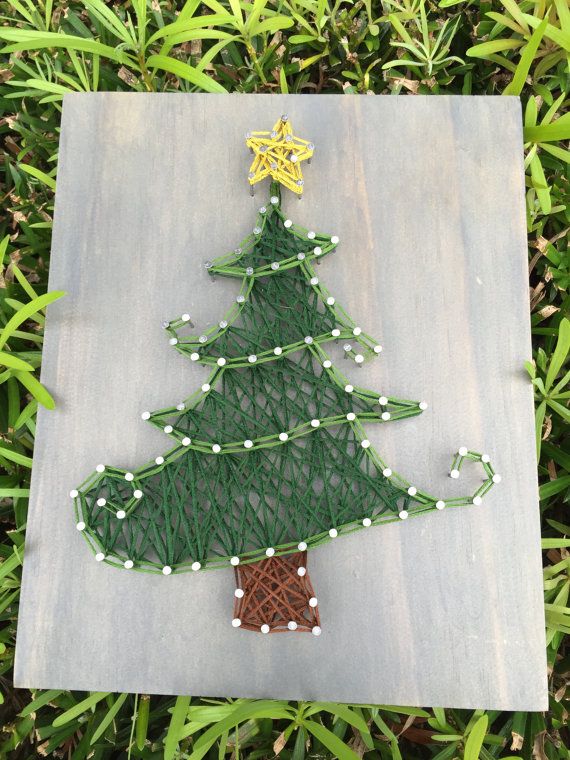 a christmas tree made out of string and beads on a piece of wood in the grass