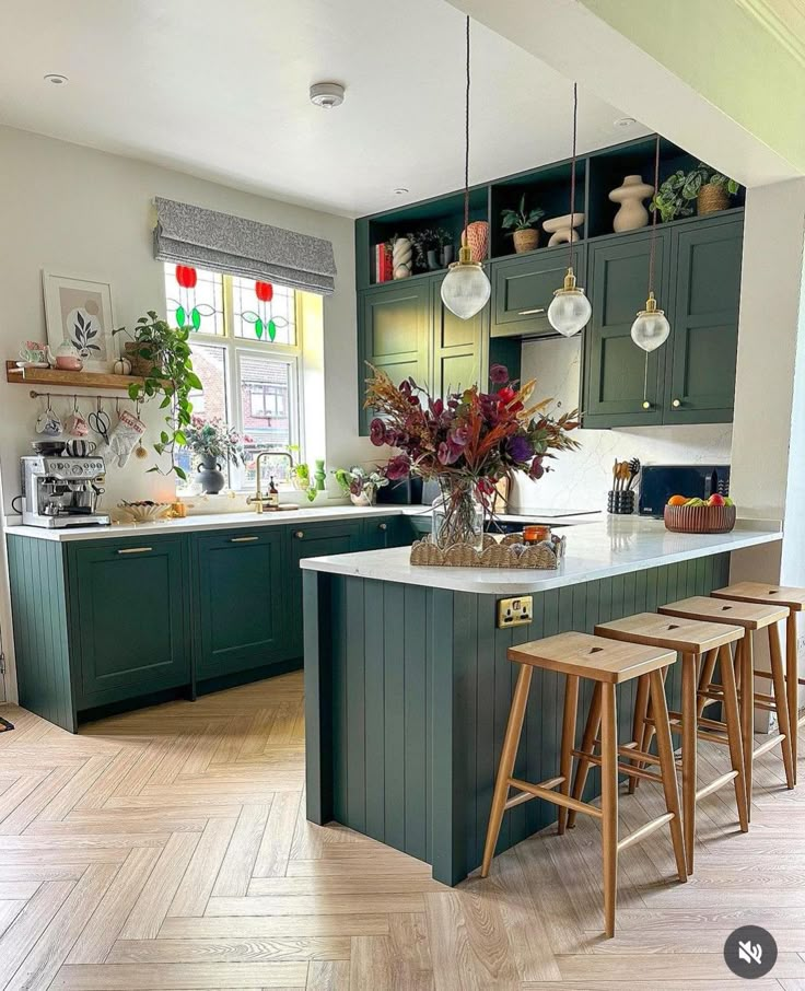 a kitchen with green cabinets and stools next to an island in front of a window