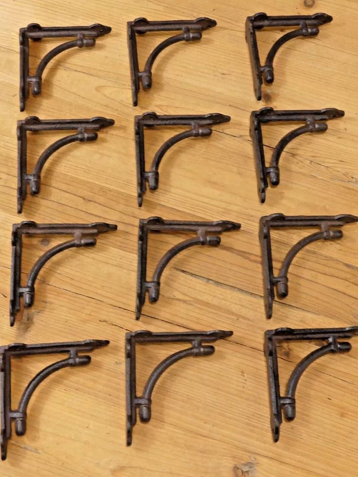 twelve antique iron shelf brackets on a wooden table with one missing the top and six in the middle