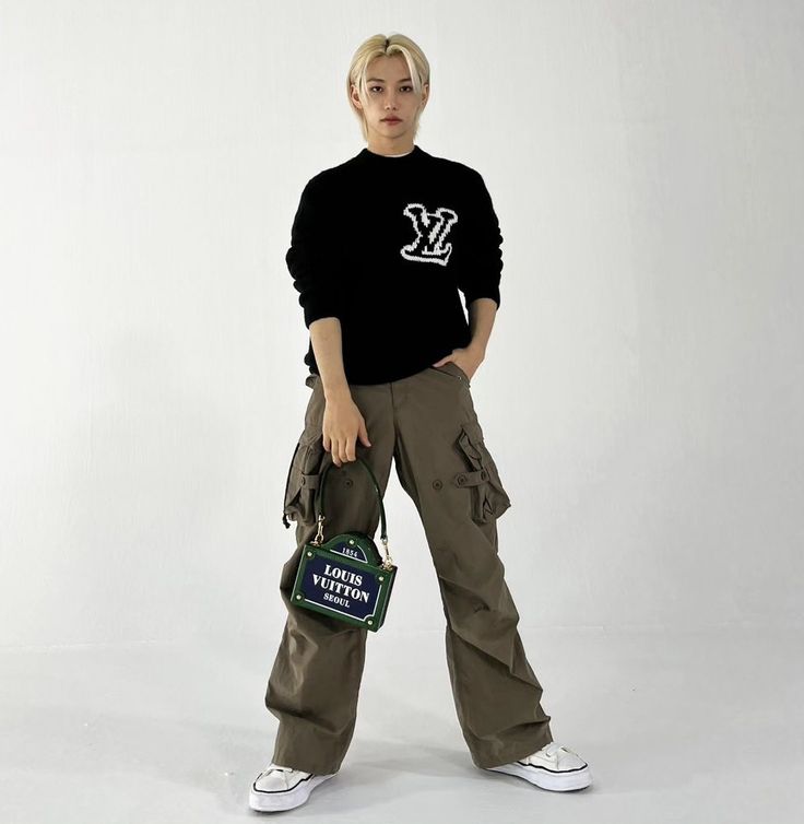 a woman standing in front of a white background wearing cargo pants and a black sweater