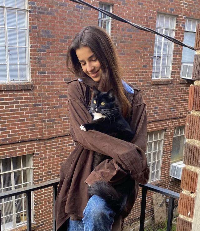 a woman holding a black and white cat on top of a balcony next to a brick building