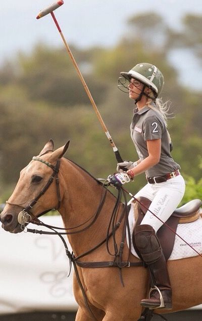 a woman riding on the back of a brown horse with a stick in her hand