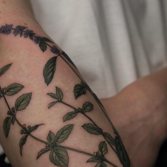 a close up of a person's arm with leaves and flowers tattooed on it