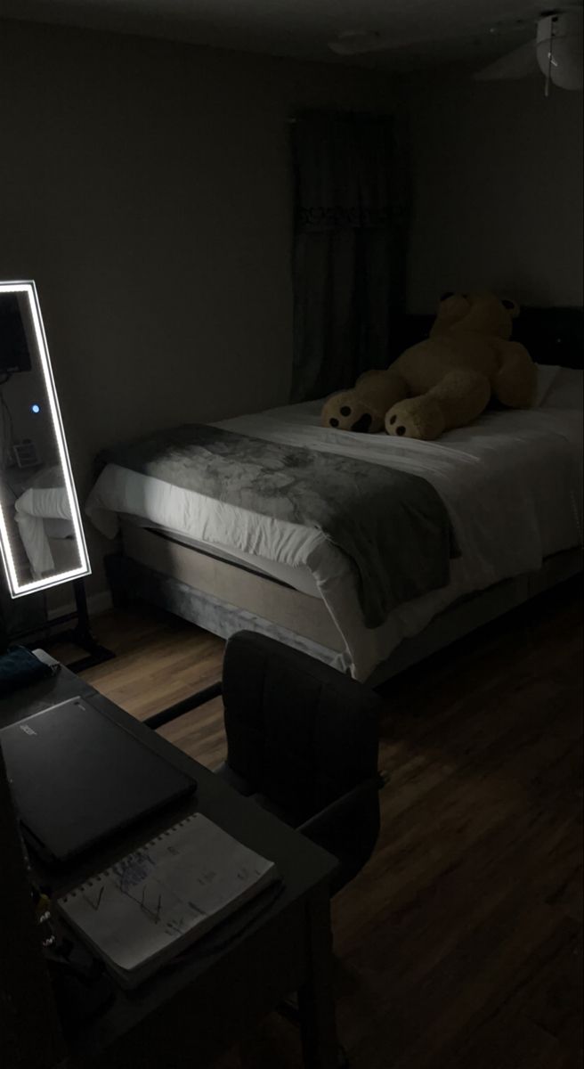 a teddy bear sitting on top of a bed next to a desk with a laptop