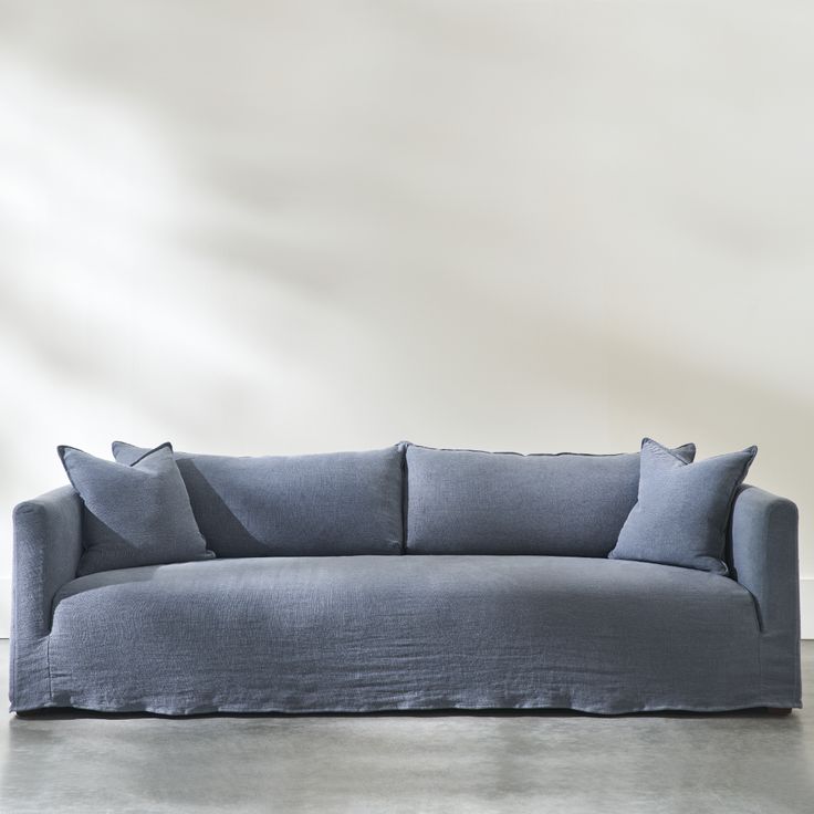 a blue couch sitting on top of a cement floor next to a white wall with three pillows